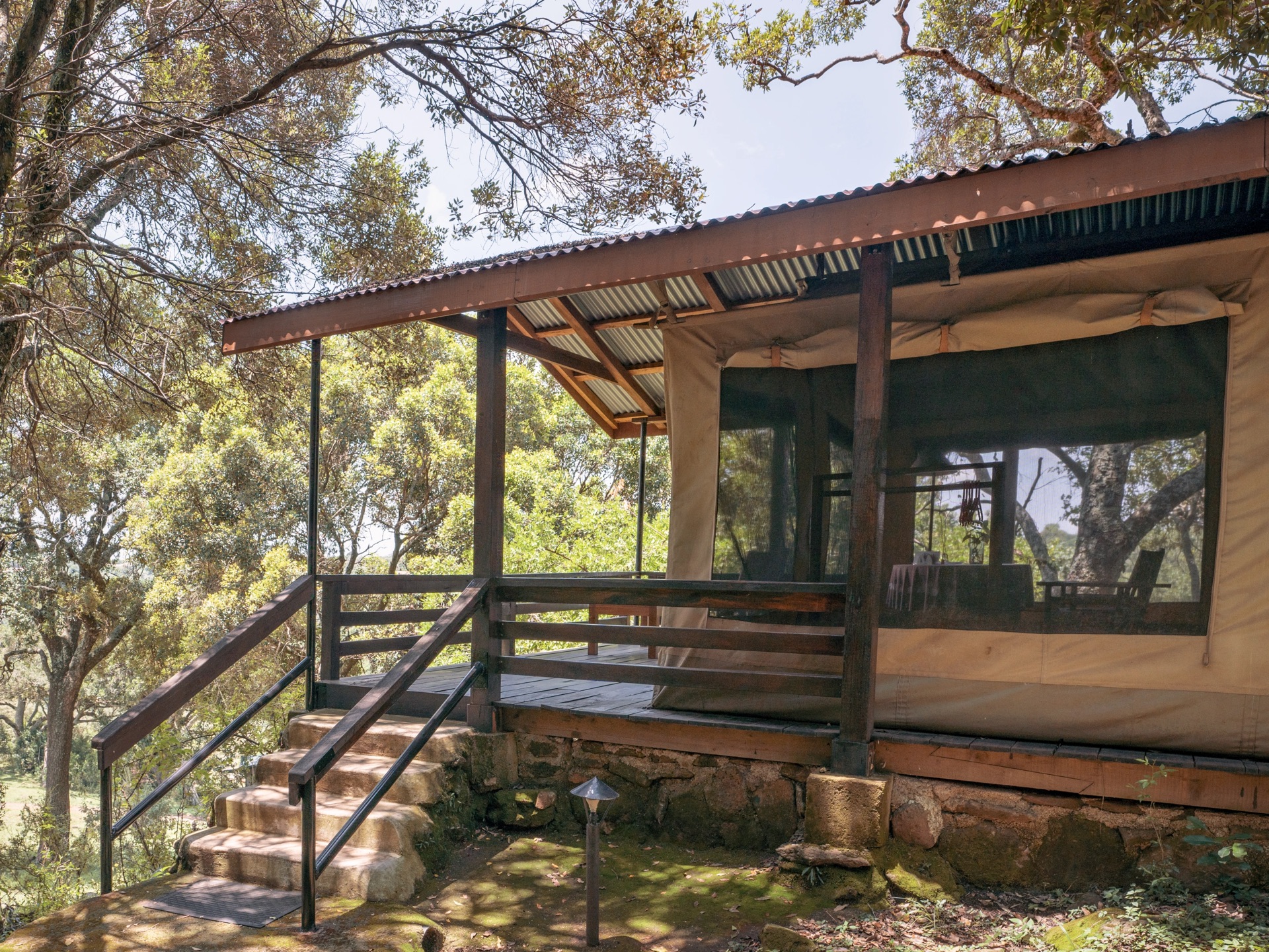 A tented room on a raised deck, with steps up to a shaded veranda