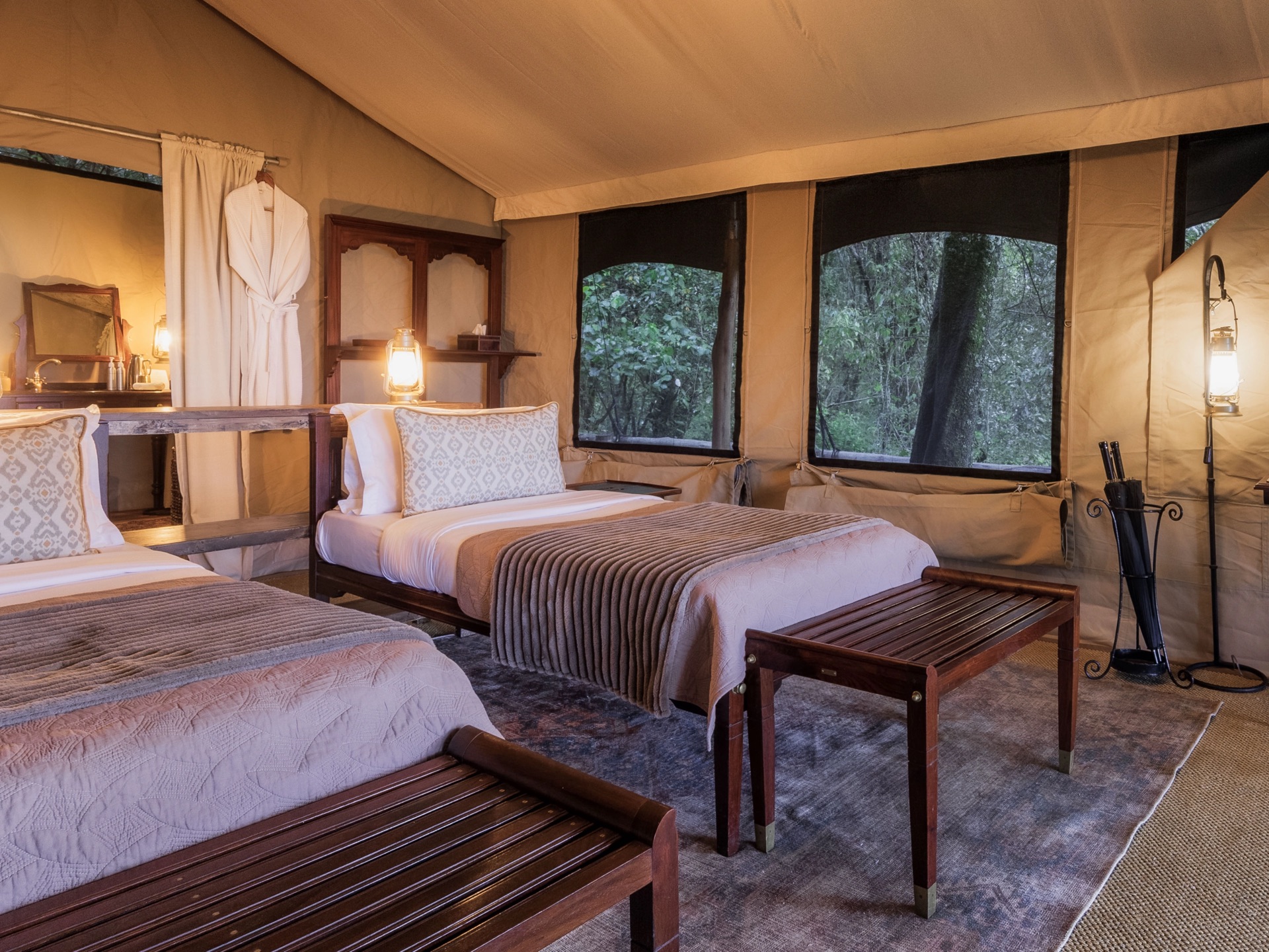 A twin-bedded tent interior with a writing desk and windows onto the bush