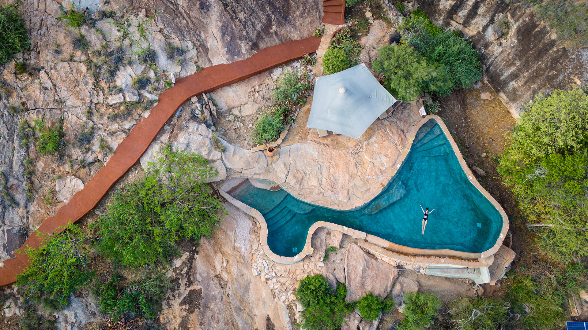 An aerial view of a pool cut into rock, with a path leading down to it
